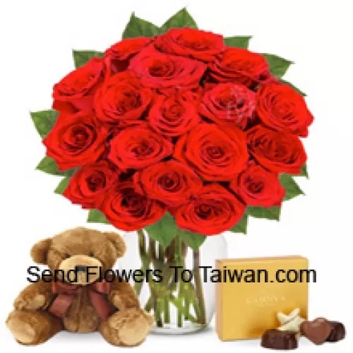 12 Rose rosse con alcune felci in un vaso di vetro accompagnate da una scatola di cioccolatini importati e da un carino orsacchiotto marrone alto 12 pollici