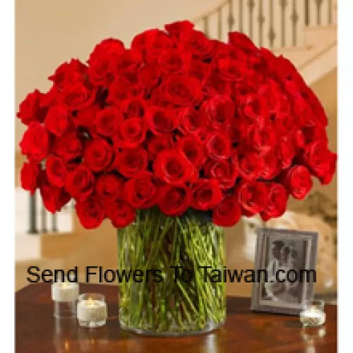 100 Roses rouges avec quelques fougères dans un grand vase en verre